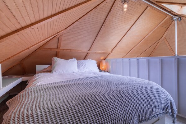A cozy bedroom with a wooden ceiling, a bed with white linens, and a textured blanket. - Small Beach Cottage near the Coastal Trail and The Ritz (Half Moon Bay)