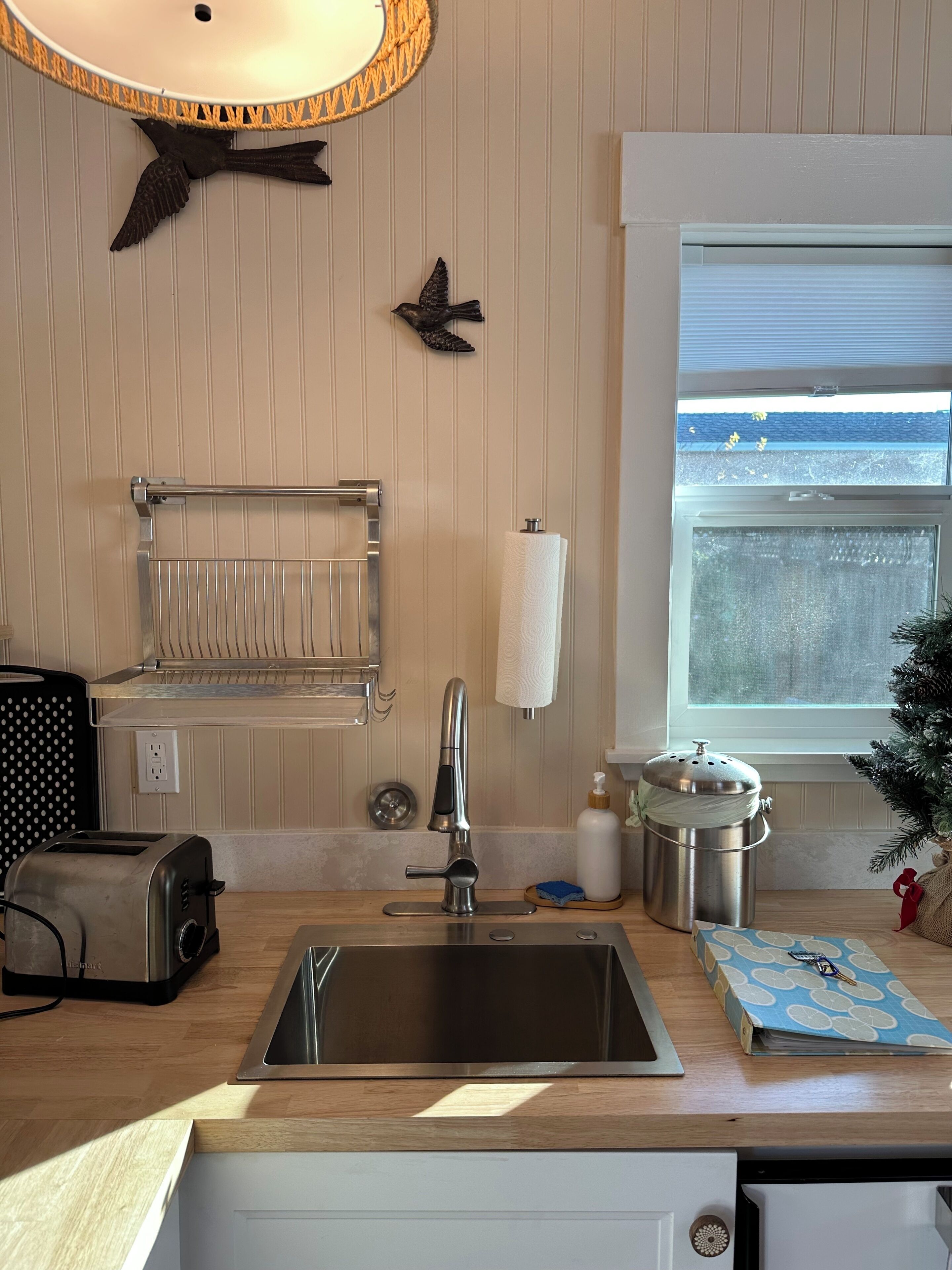 A kitchen with a stainless steel sink, a toaster, a hanging towel rack, and a window with a view of the sea.