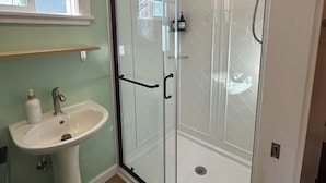 A bathroom with a glass-enclosed shower, a pedestal sink, and a window with blinds. - Small Beach Cottage near the Coastal Trail and The Ritz (Half Moon Bay)