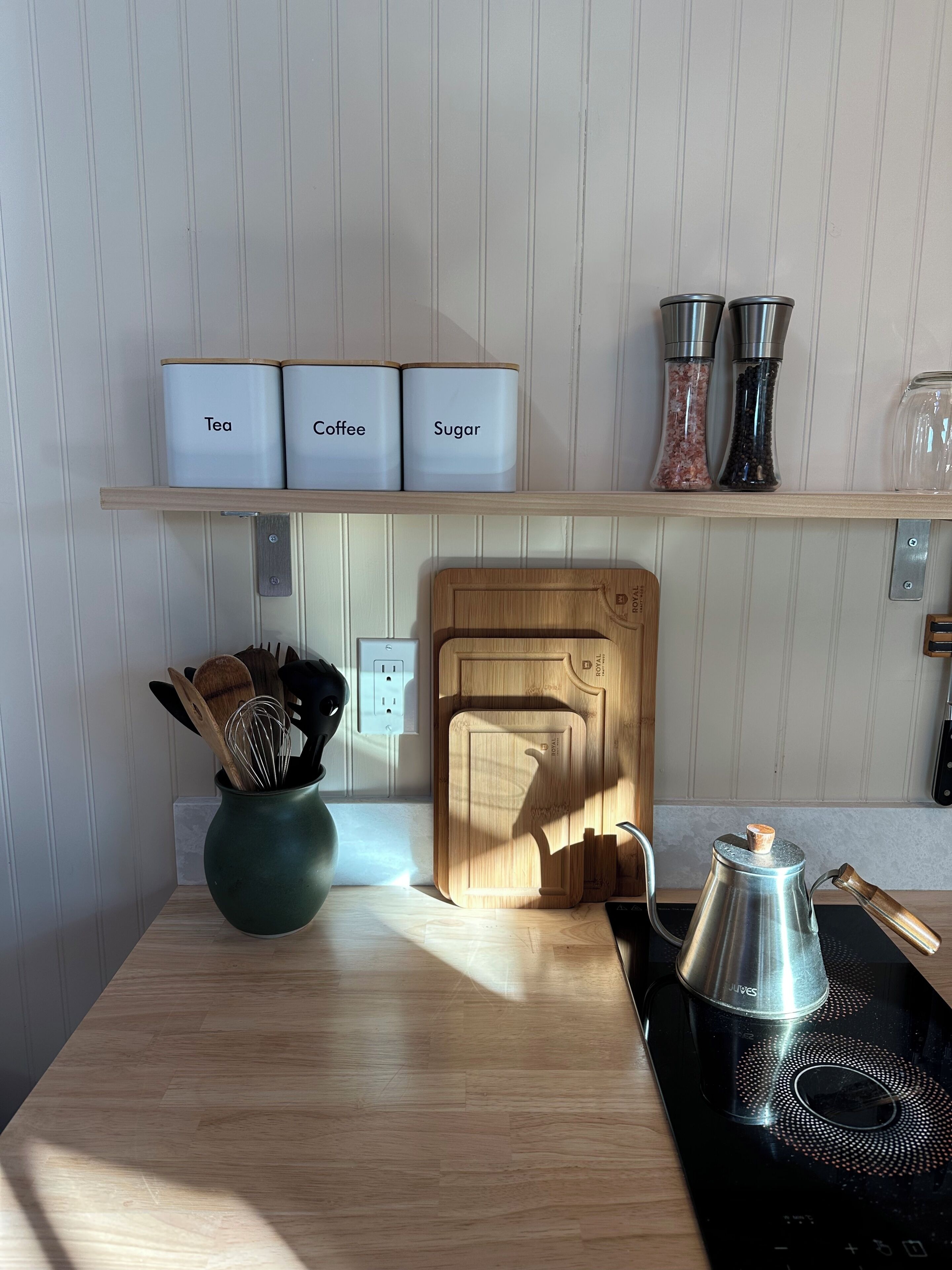 A kitchen with a wooden cutting board, a kettle, and labeled containers for tea, coffee, and sugar.
