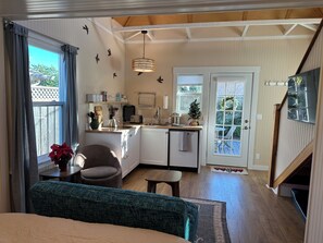 A compact kitchen with a dining area, a small seating space, and a staircase leading to an upper level. - Small Beach Cottage near the Coastal Trail and The Ritz (Half Moon Bay)