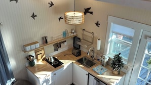 A compact kitchen with white cabinets, a wooden countertop, a hanging light fixture, and a window with a view. - Small Beach Cottage near the Coastal Trail and The Ritz (Half Moon Bay)