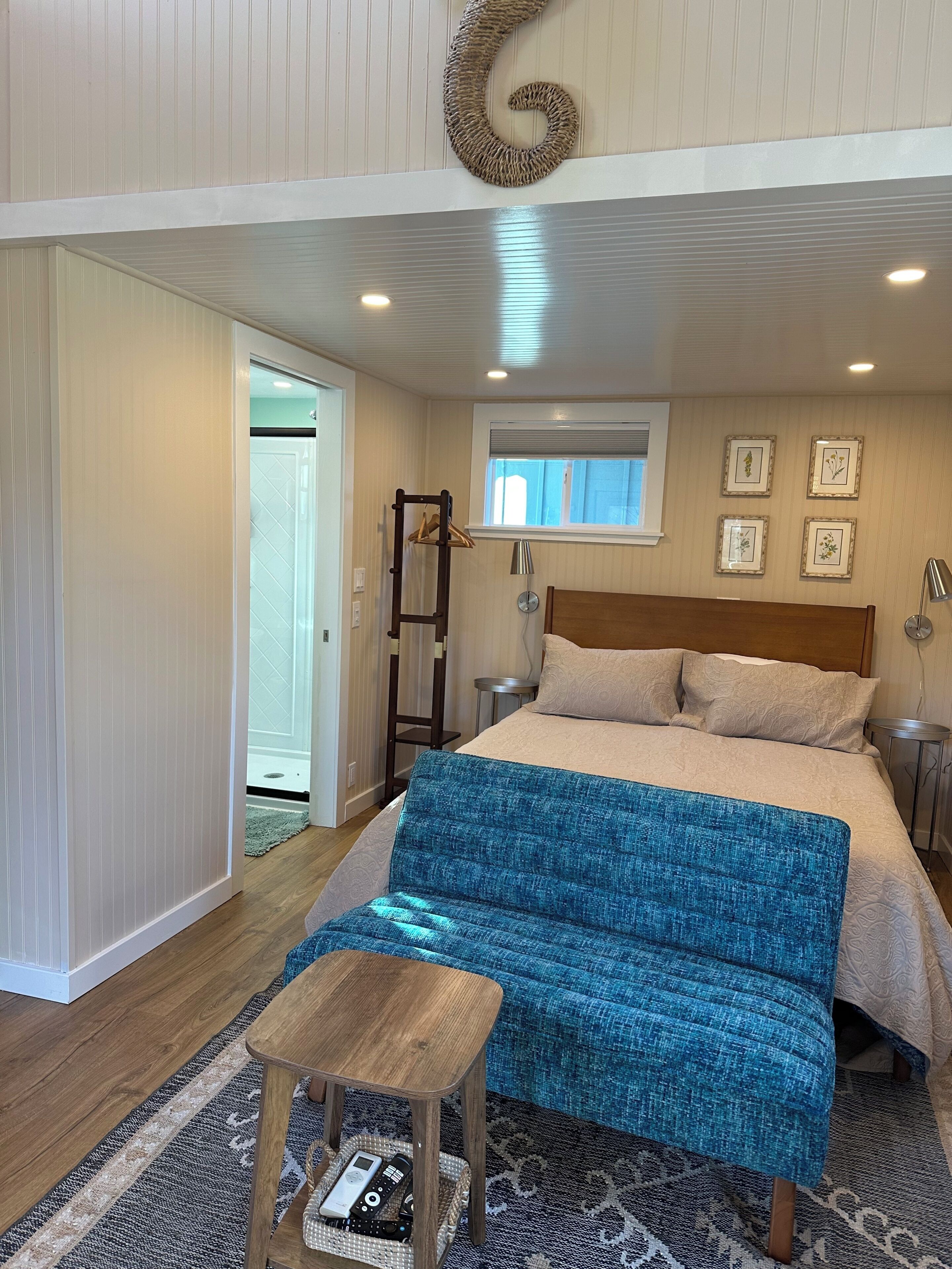 A bedroom with a bed, bedside tables, a hanging light fixture, a window, and a door.