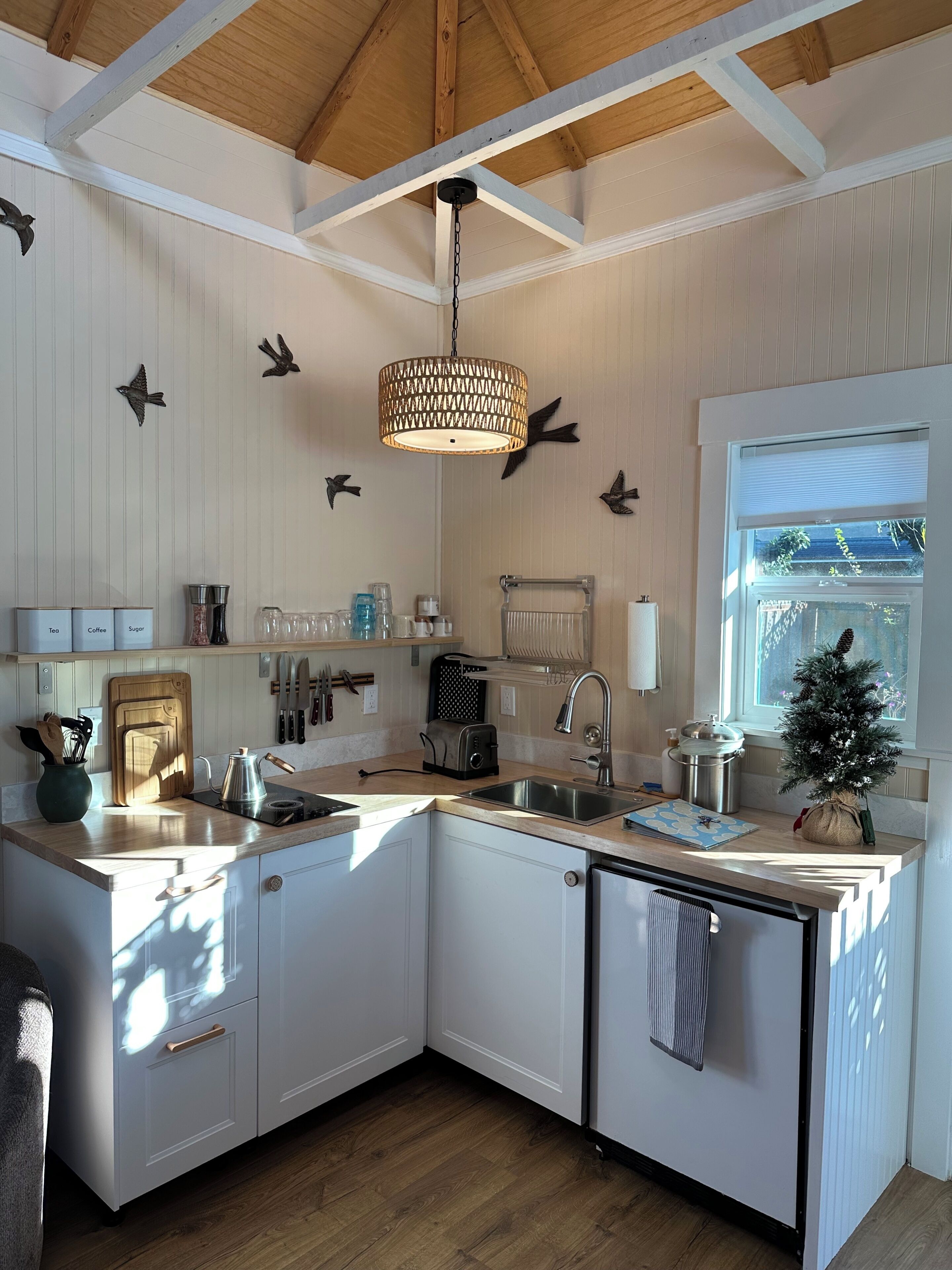 Une cuisine avec des meubles blancs, un plafond en bois, un luminaire suspendu et une fenêtre donnant sur un beau paysage.