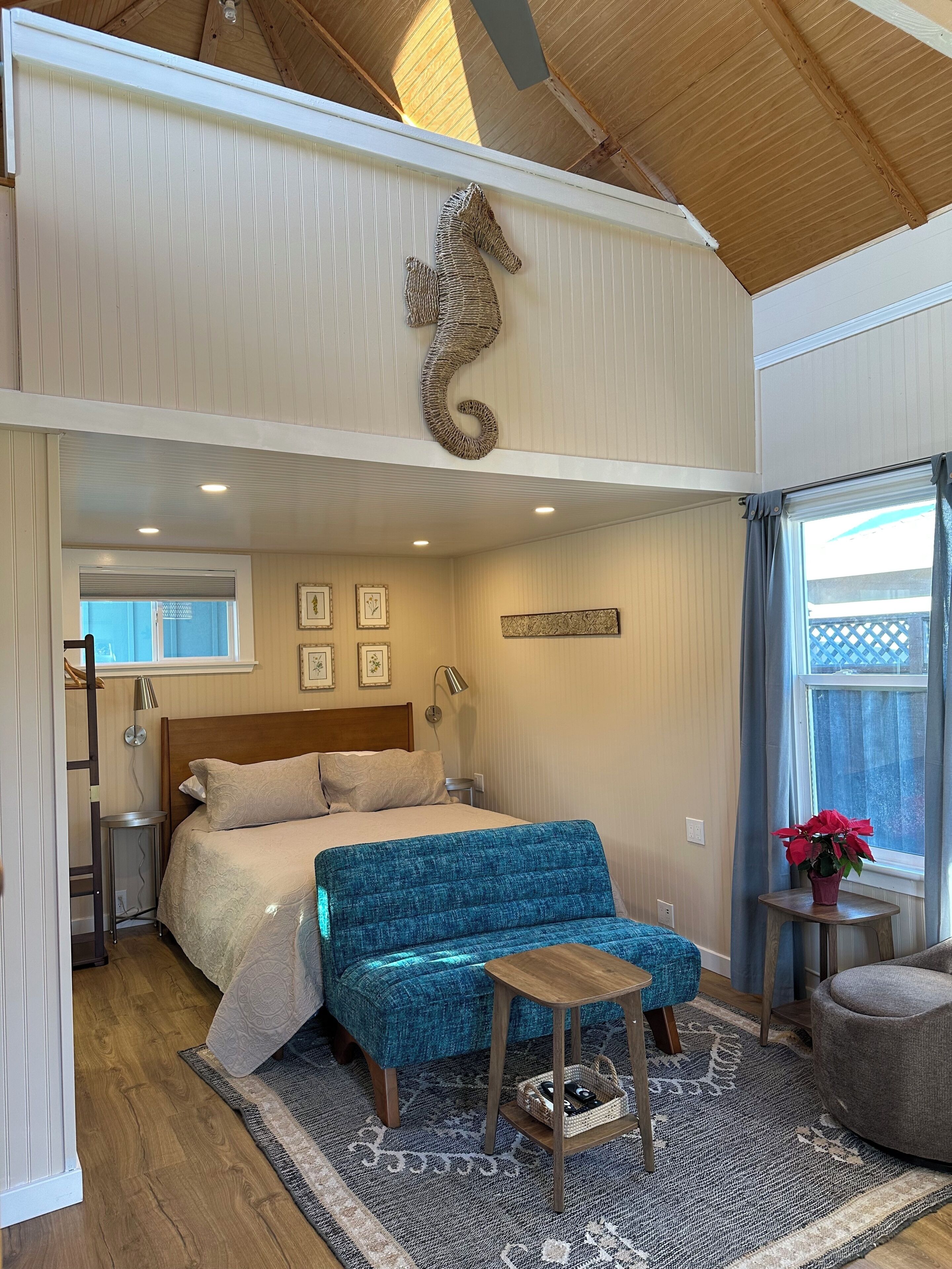Una camera da letto con un letto, una panca imbottita blu, un piccolo tavolo di legno e un decorativo arazzo a forma di cavalluccio marino.