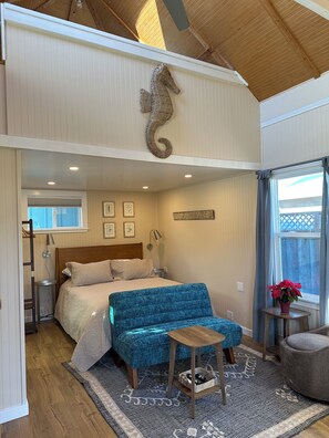 A bedroom with a bed, a blue upholstered bench, a small wooden table, and a decorative seahorse wall piece. - Small Beach Cottage near the Coastal Trail and The Ritz (Half Moon Bay)