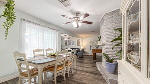 A dining area with a white table and chairs, a ceiling fan, and a brick accent wall. - POOL House on the Kemah Boardwalk w BIKES (Kemah)