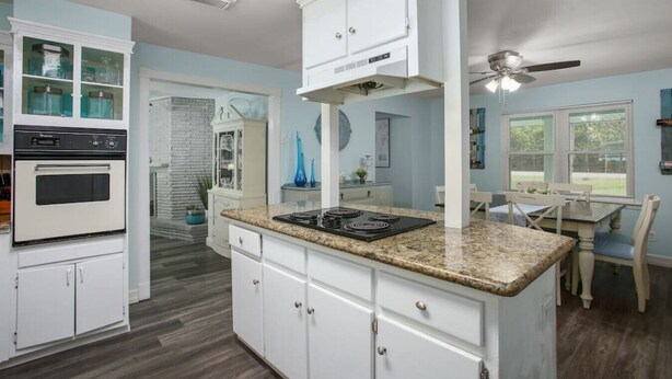 A kitchen with white cabinets, a built-in oven, a granite countertop, and a dining area with a table and chairs. - POOL House on the Kemah Boardwalk w BIKES (Kemah)