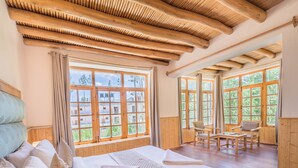 Une pièce avec un plafond en bois, de grandes fenêtres, un lit avec du linge de maison blanc et un coin salon avec des fauteuils.