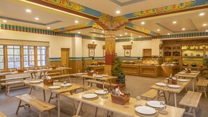 Une salle à manger avec des tables et des bancs en bois, un pilier décoratif central et un espace buffet proposant divers plats.