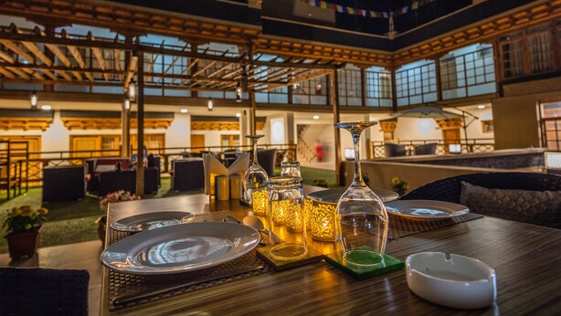 Un espace repas avec des tables disposées pour accueillir quatre personnes, entouré d’un haut plafond orné de poutres en bois et offrant une vue sur le jardin en contrebas.