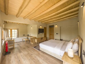 A room with a large bed, a desk, a chair, a radiator, a TV, and a window with curtains.