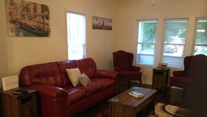 A living room with a red leather sofa, a wooden coffee table, and a red armchair. There is a painting on the wall and a window with blinds. - Charming! Near Microsoft Mt Pleasant - Sleeps 8 (Kenosha)