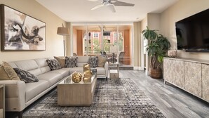 A modern living room with a sofa, coffee table, and TV. There is a ceiling fan, a large painting, and a plant. - Bayfront - in the Heart of Naples!  (Naples)