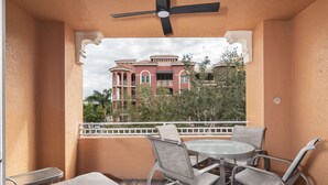A balcony with a table and chairs, a ceiling fan, and a view of a large building with red and white architecture. - Bayfront - in the Heart of Naples!  (Naples)