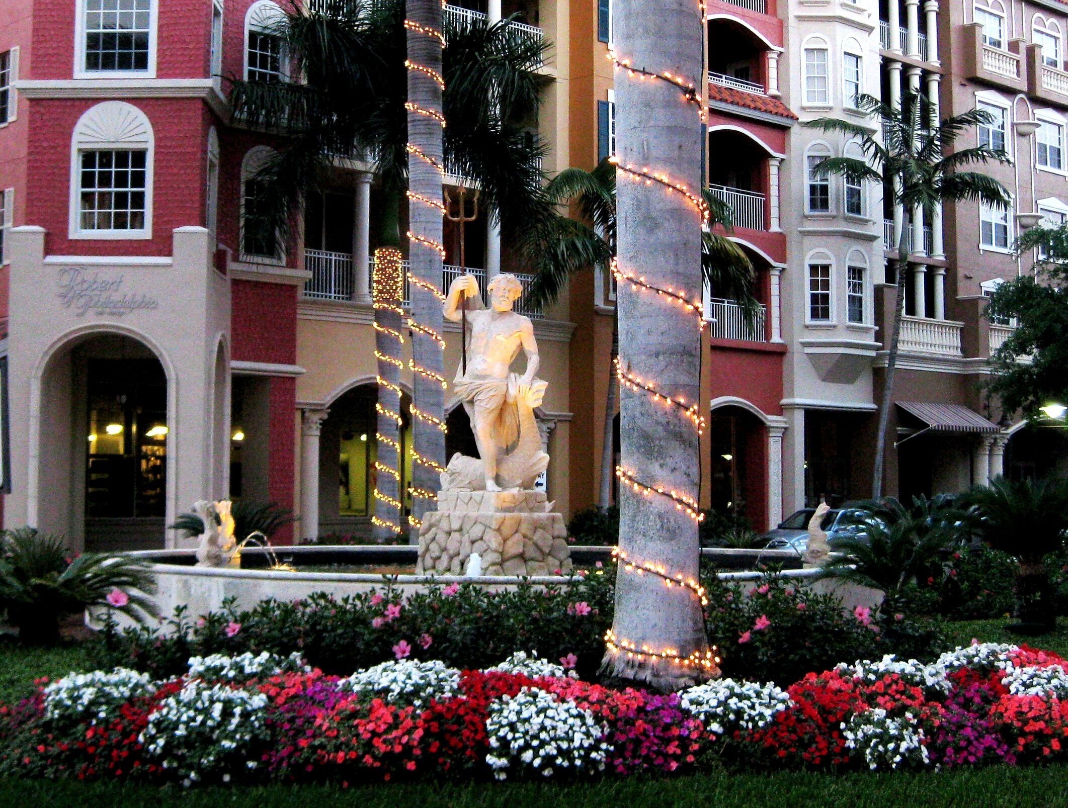 A statue in a garden with a building in the background.