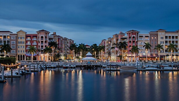 A marina with boats docked, surrounded by multi-story buildings with balconies and palm trees. - Bayfront - in the Heart of Naples!  (Naples)