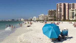A beach with high-rise buildings in the background, a clear sky, and people enjoying the beach. - Bayfront - in the Heart of Naples!  (Naples)