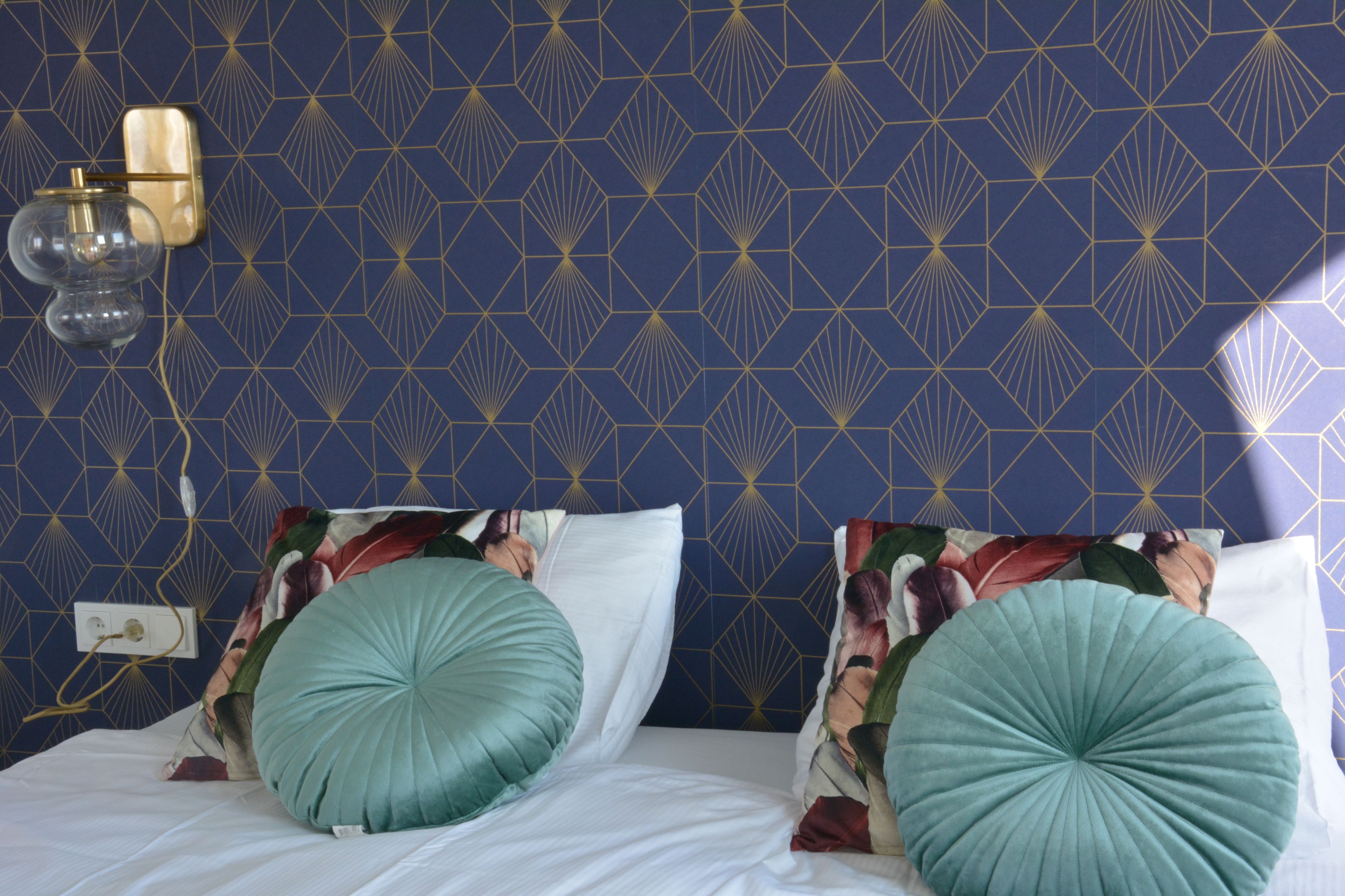 A bedroom with a patterned wallpaper, two large pillows, and a wall-mounted light fixture.
