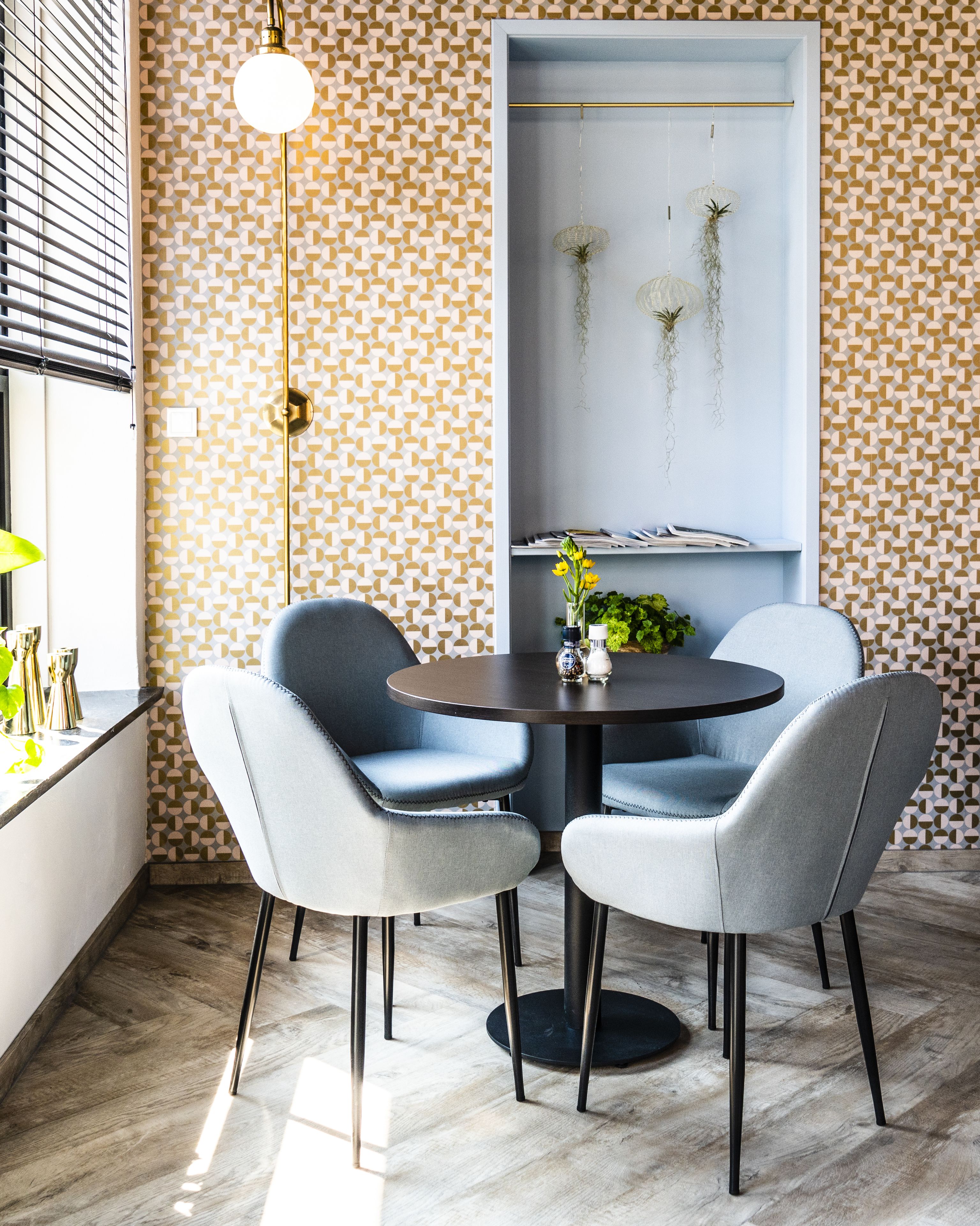 Uma sala de jantar moderna com uma mesa redonda, duas cadeiras cinzas estofadas e um vaso com flores amarelas.