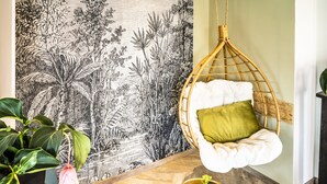 Una habitación con una silla colgante, una mesita redonda y dos sillones estampados.