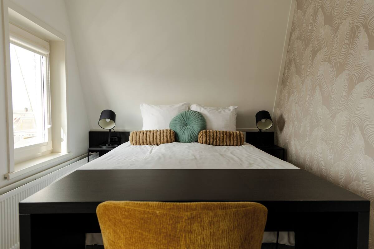 A bedroom with a bed, two bedside tables, a desk, and a chair.