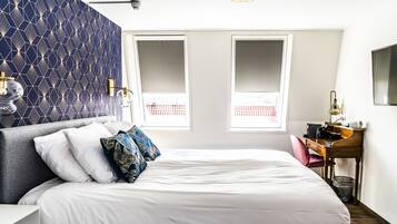 A neatly arranged bedroom with a large bed, a desk, and a chair, featuring a geometric patterned wall and a window with a view.