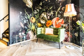 Una habitación con un sofá verde, una lámpara de pie y un mural floral en la pared.