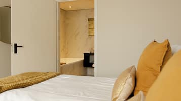 Ein Schlafzimmer mit Bett, Nachttisch und einem durchgehenden Türrahmen sichtbarem Badezimmer.