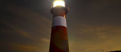 A lighthouse at night with a bright light at the top, set against a starry sky.