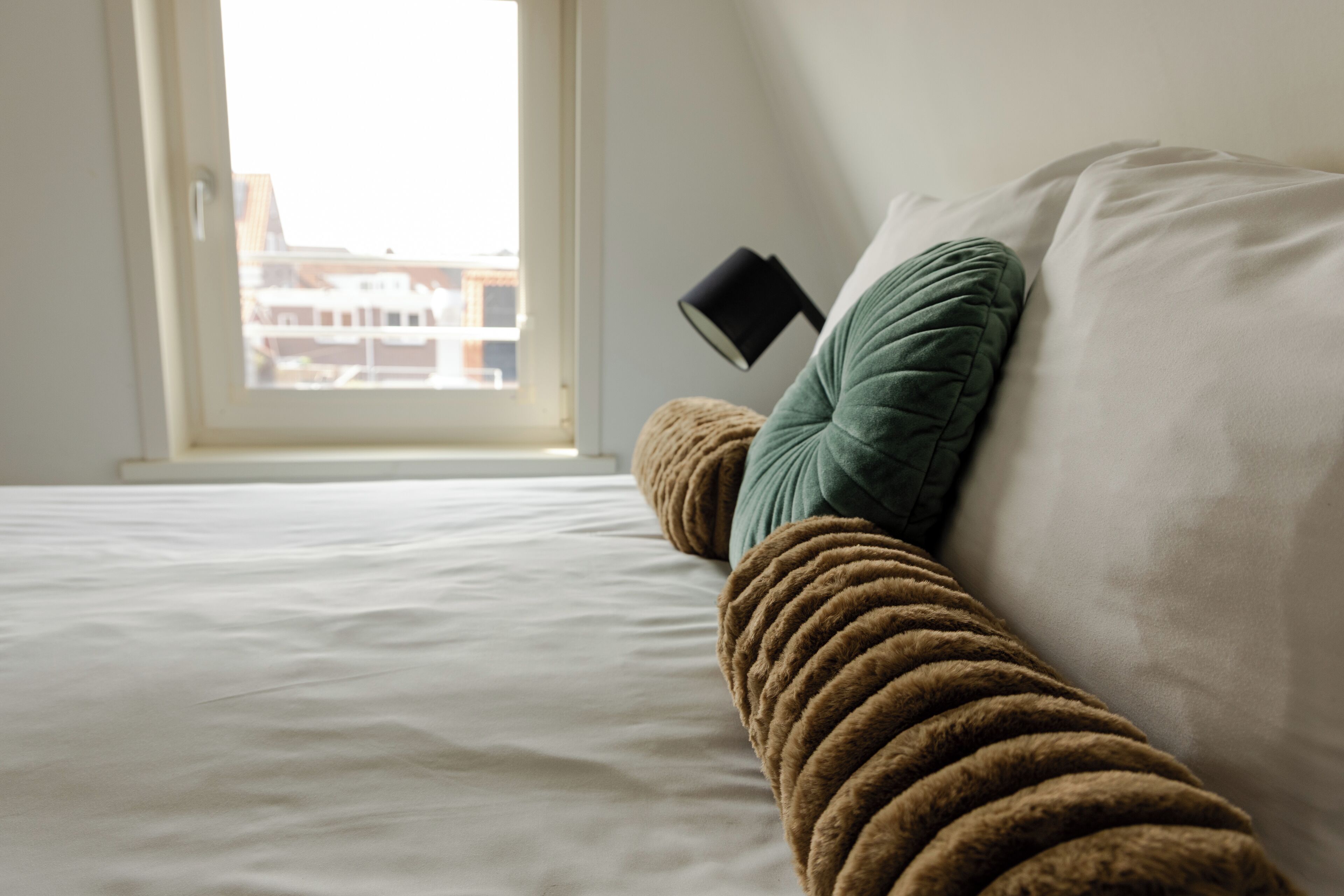 A bed with a view of buildings through a window.