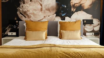 A bed with a gold textured blanket and pillows, a large floral artwork on the wall, and bedside tables with lamps.