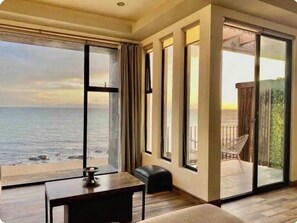 Una habitación con un amplio ventanal con vistas al mar, una puerta corrediza de vidrio a un espacio exterior y una pequeña mesa con una vela.