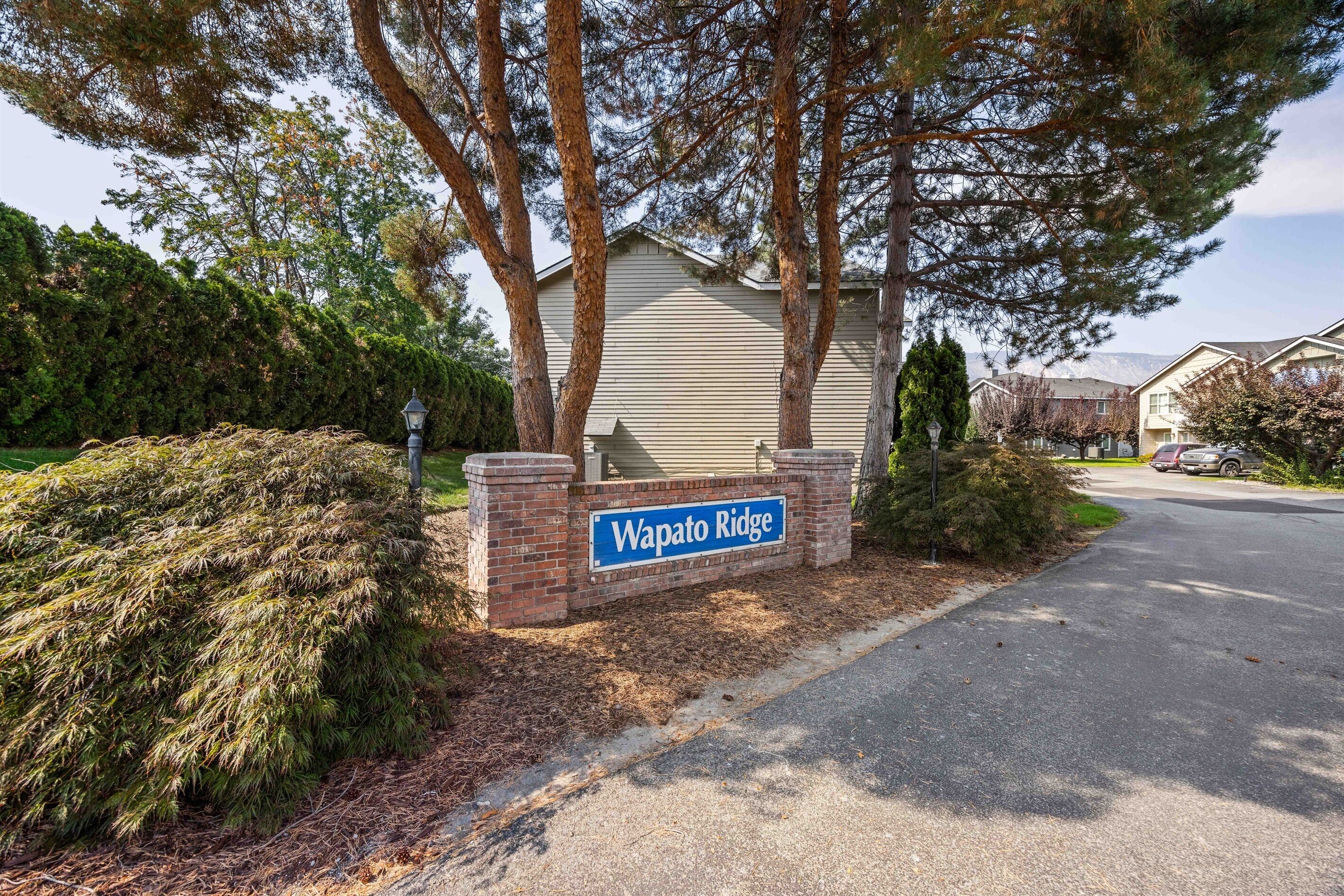 A sign for Wapato Ridge with a paved driveway and surrounding trees.