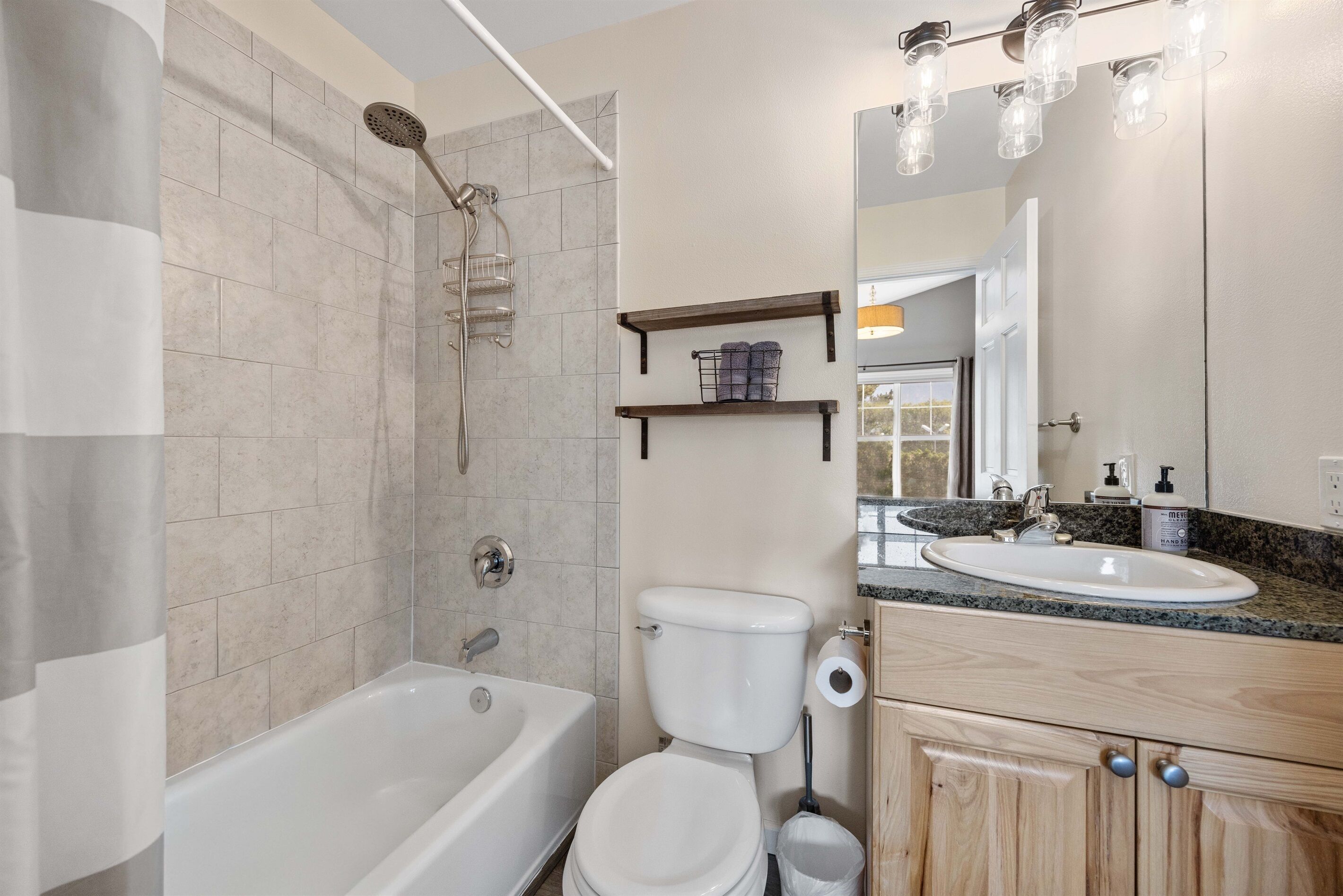 Ein modernes Badezimmer mit Badewanne, Toilette und Waschbecken. Über dem Waschbecken befinden sich Regale und über der Badewanne eine Duschbrause.