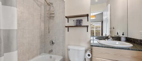 Ein modernes Badezimmer mit Badewanne, Toilette und Waschbecken. Über dem Waschbecken befinden sich Regale und über der Badewanne eine Duschbrause.