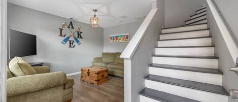 A living room with a sofa, a wooden chest, a flat-screen TV, and a staircase.