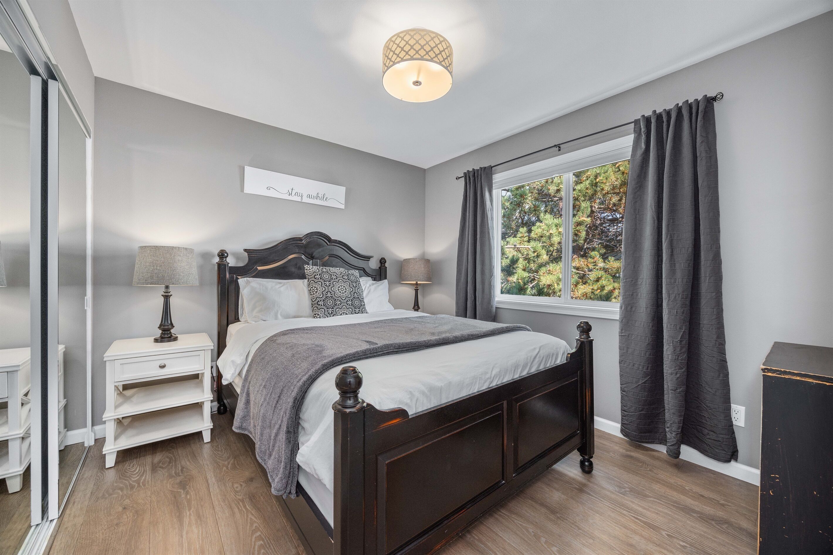 Un dormitorio con cama, mesitas de noche, ventana con cortinas e iluminación en el techo.