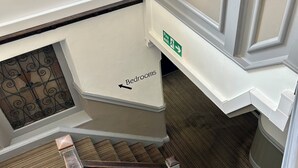Un intérieur à plusieurs niveaux, avec un escalier menant à un étage inférieur, un panneau indiquant la sortie de secours et un autre panneau indiquant la direction des chambres.