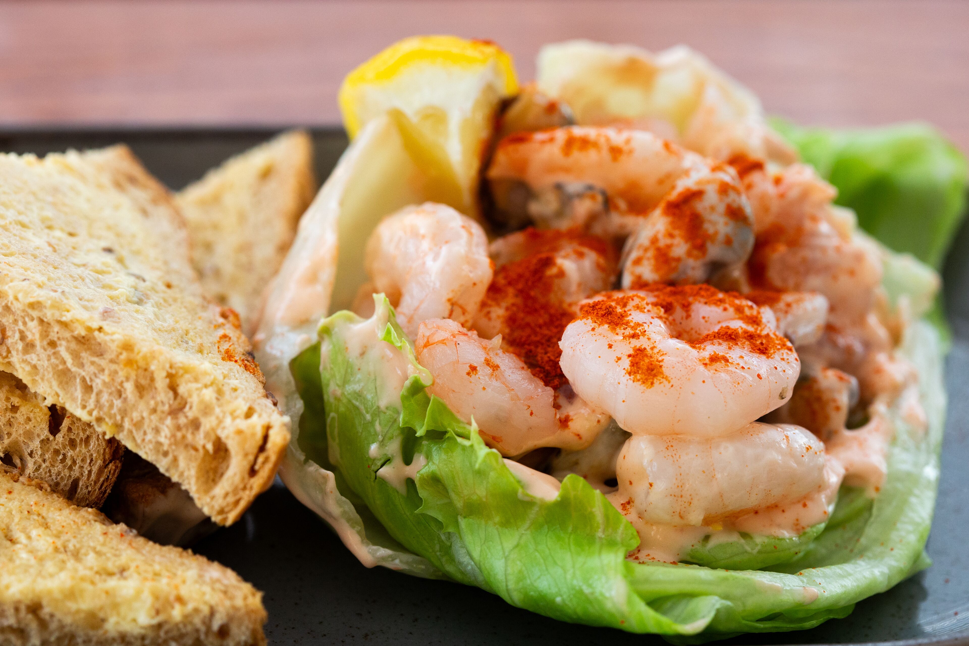 A seafood dish with shrimp, lettuce, and a lemon wedge on a plate.
