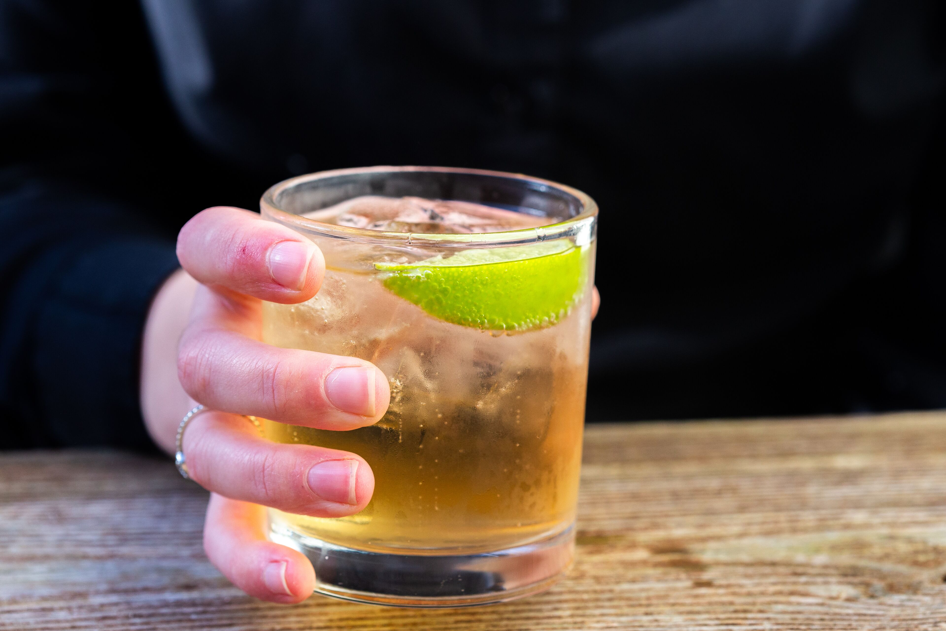 A hand holding a glass with a lime wedge.