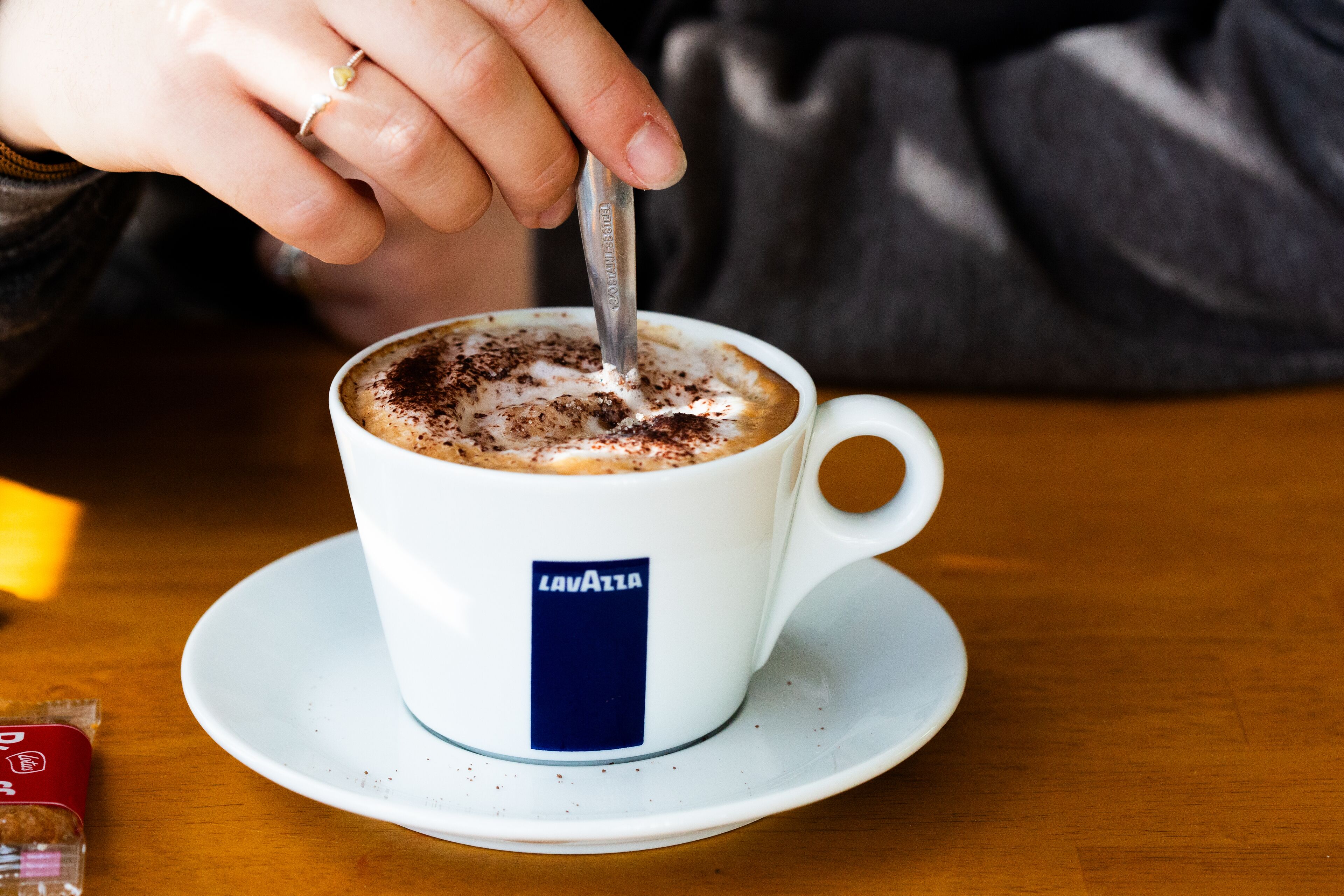 A cup of coffee with a spoon, a saucer, and a blue label on the cup.