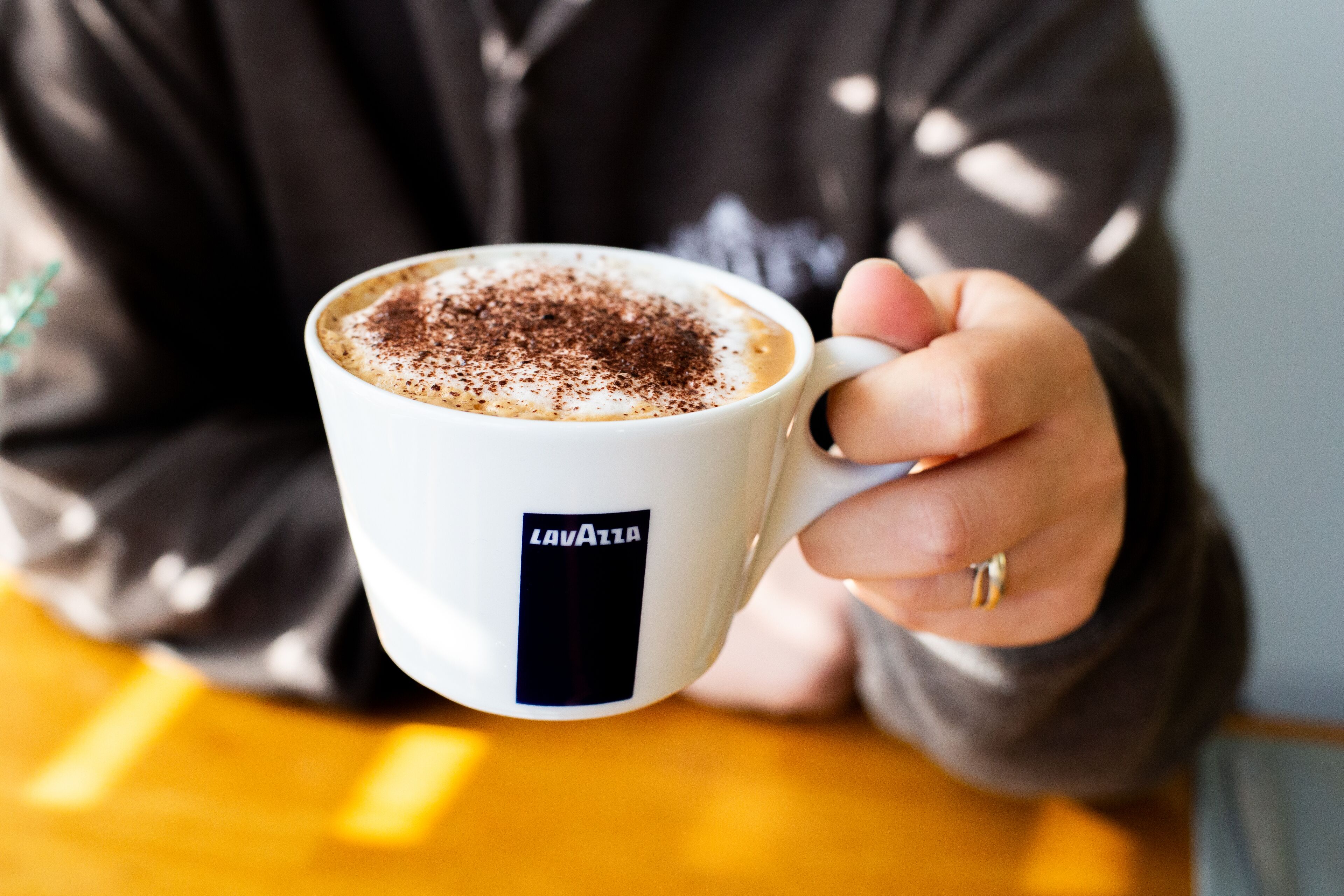 Una persona sosteniendo una taza blanca con una etiqueta negra que dice 'LAVVIA'.