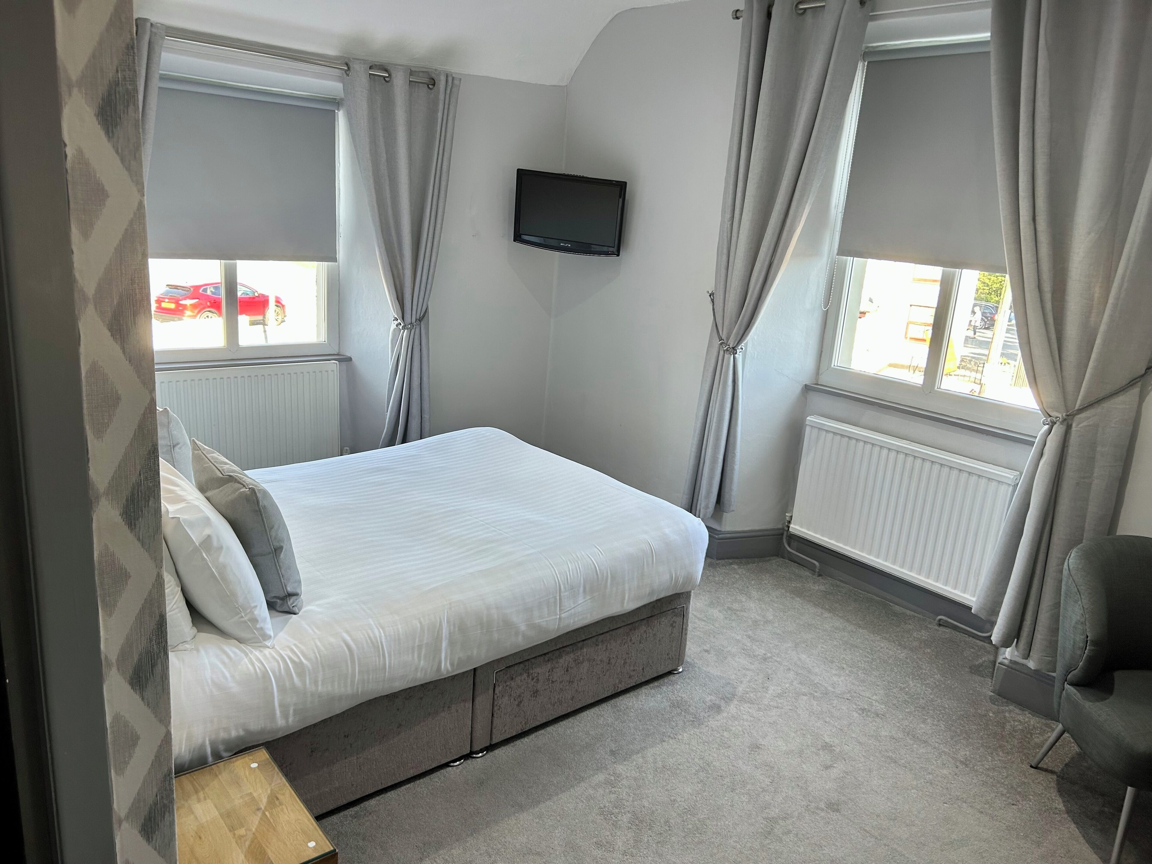 A bedroom with a bed, a TV, and a window with curtains.