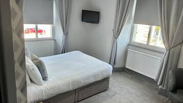 A bedroom with a bed, a TV, and a window with curtains.