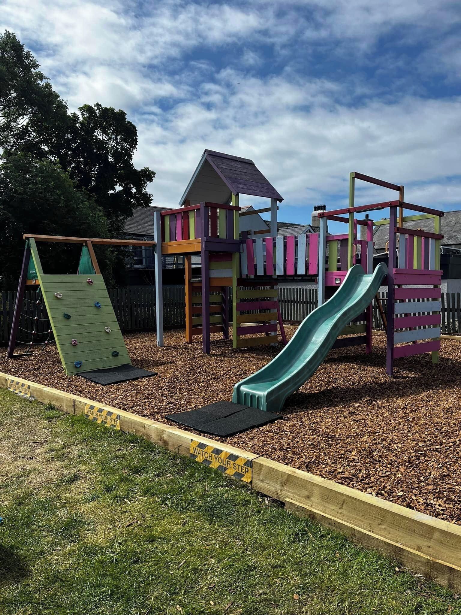 Un patio de juegos con una pared de escalar, un tobogán y una casita.