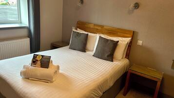 A neatly made bed with a folded towel and a food voucher, a bedside table, and a nightstand.