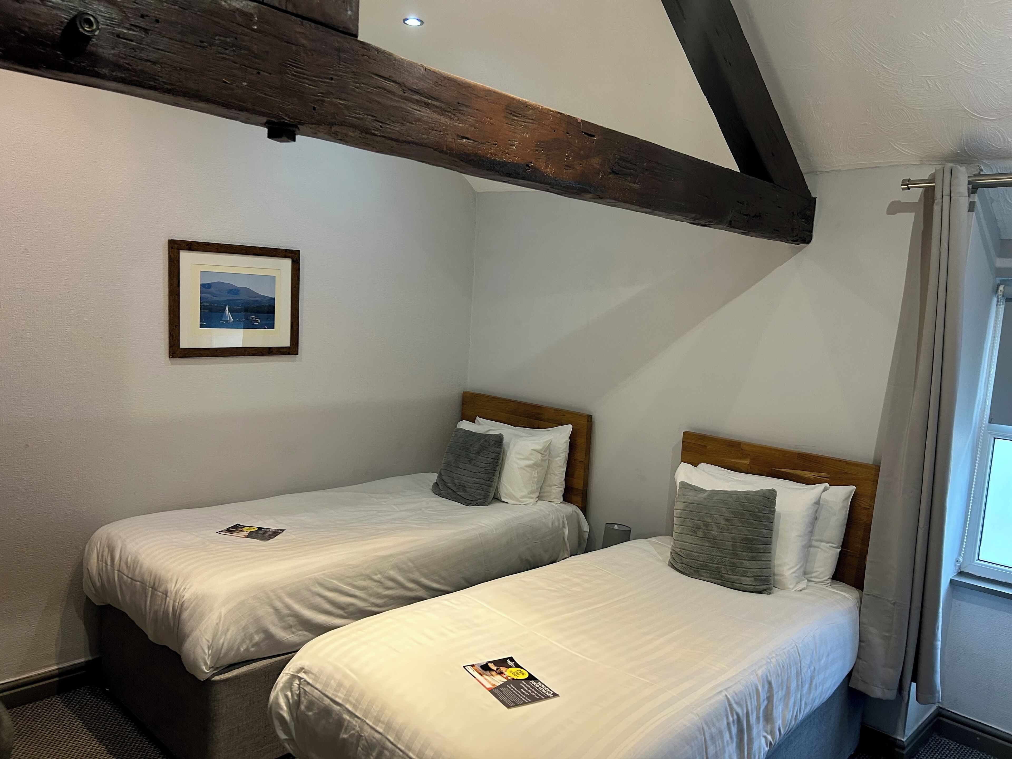 A bedroom with two single beds, wooden headboards, a framed picture on the wall, and a window with curtains.