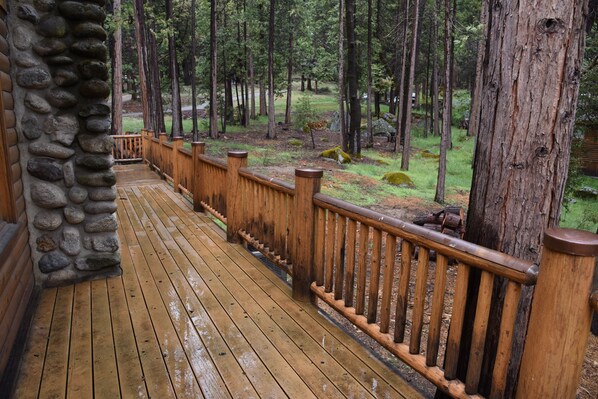 A wooden deck with a stone wall on one side, surrounded by a forested area.