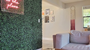 Ein Wohnzimmer mit grüner Wand, einer Neonreklame, einem Sofa, einem Couchtisch und einem gemusterten Teppich.